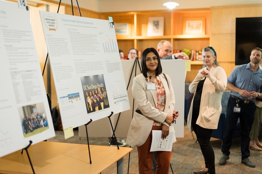 Award winner standing beside their project board titled 'Population Health Wellness Outreach Hub' at the 2024 Improvement Excellence Awards at UC San Diego Health.